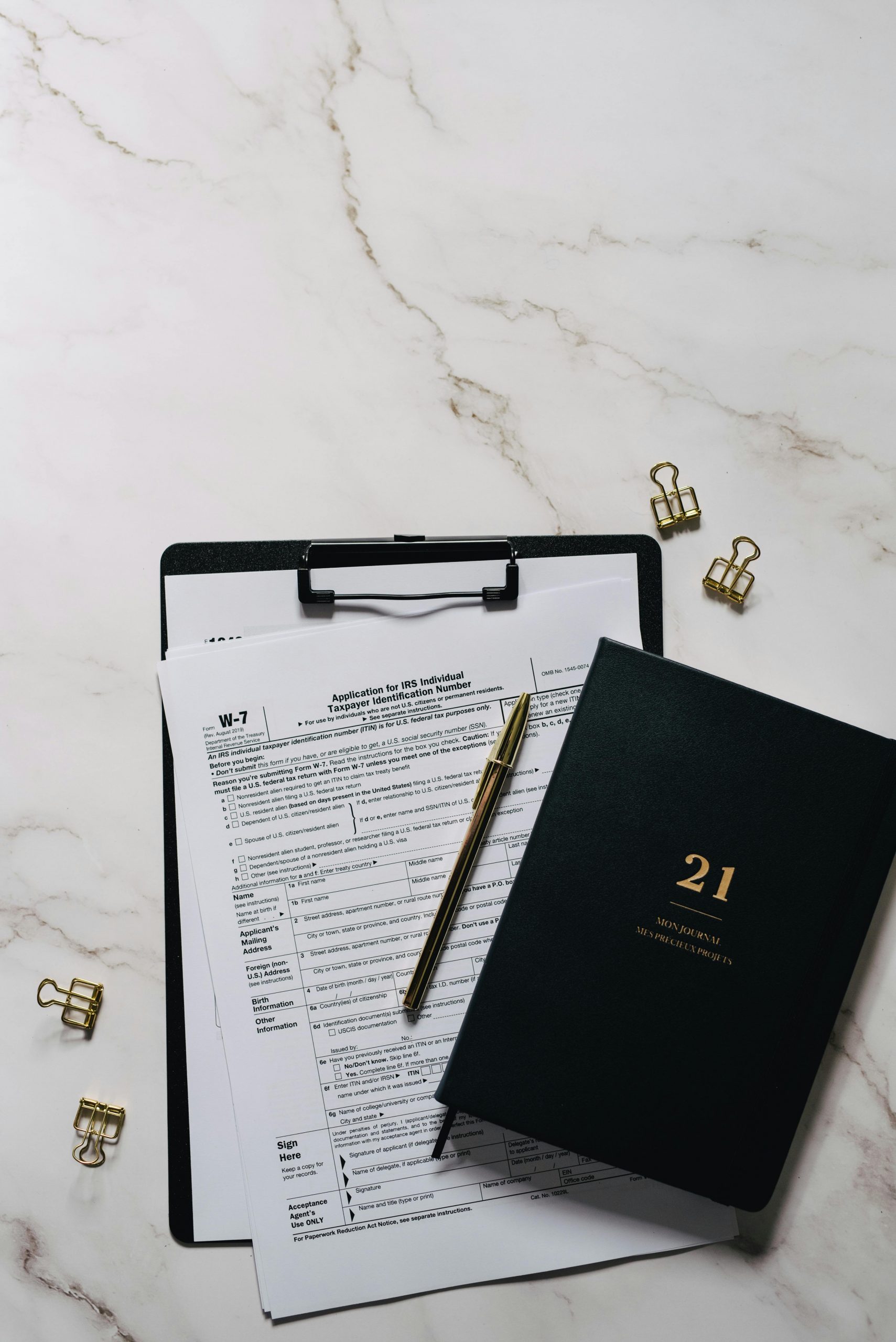 Flat lay of a clipboard with documents and a notebook on marble.